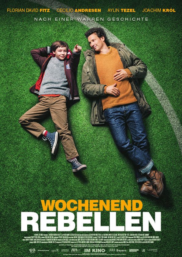 Filmplakat: Die Wochenendrebellen - Ein Mann und ein Kind liegen auf dem Rasen eines Fußballstadions